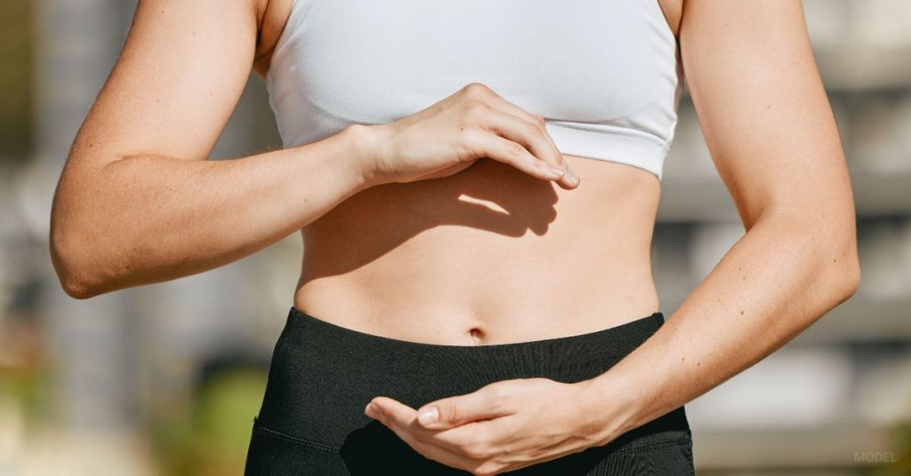 Woman (MODEL) holding her hands around her stomach proud of her tummy tuck results